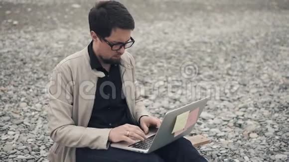 年轻的商人正在用笔记本电脑在岩石海滩上开发一家初创公司视频的预览图