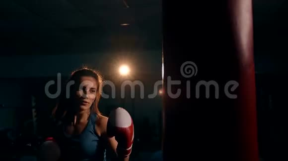 一个漂亮的女人对一个拳击袋进行猛烈的打击手持射击视频的预览图
