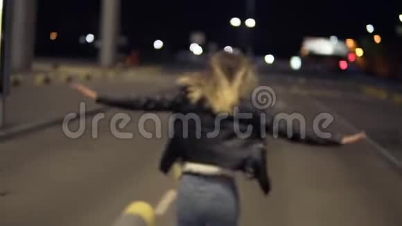 快乐的金发女人晚上在户外玩得很开心在机场大楼附近跑步模仿飞机跳跃视频的预览图