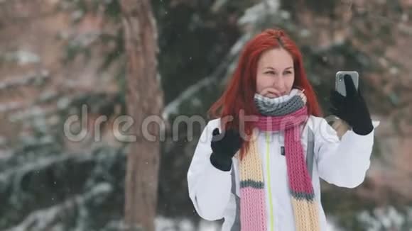 冬季公园一个头发鲜红的女人站在雪树前抚摸着她的头发视频的预览图