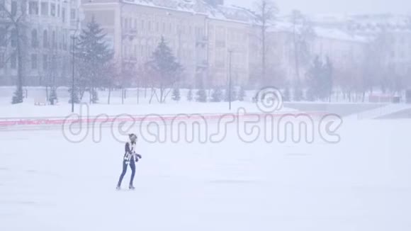 一个年轻的女人独自在外面的露天溜冰场滑冰大雪纷飞视频的预览图