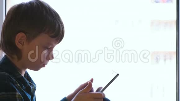 活泼的男孩正坐在窗台上用平板电脑学习科目视频的预览图
