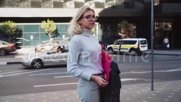 戴着眼镜的年轻女学生手拿着文件夹站在城市大街上视频的预览图