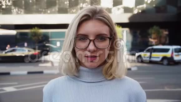 年轻快乐的女学生戴着眼镜微笑着面对城市街道视频的预览图