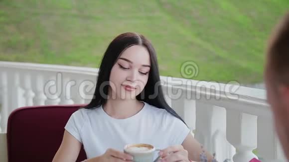 一个非常漂亮的女孩在餐厅的露天露台上喝卡布奇诺视频的预览图
