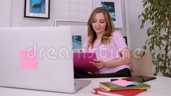 一个漂亮迷人的女孩穿着一件粉红色的t恤金发碧眼穿着一件明亮的笔记本电脑视频的预览图