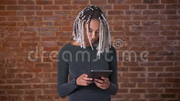 年轻的非洲女孩带着可怕的东西用平板电脑看着相机微笑着砖墙里视频的预览图