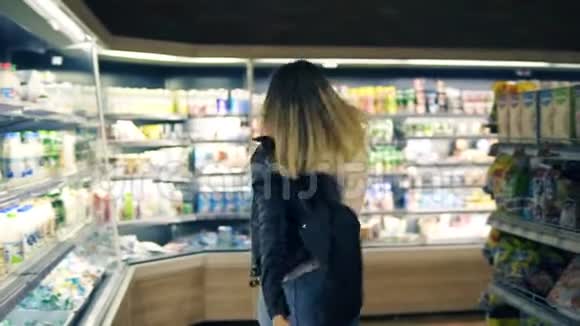 在超市快乐的年轻女人在货架上的商品和奶制品中跳舞把她的黑色夹克脱掉视频的预览图