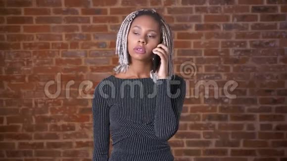 年轻的非洲女孩带着可怕的公鸡在电话里说话背景是砖墙视频的预览图