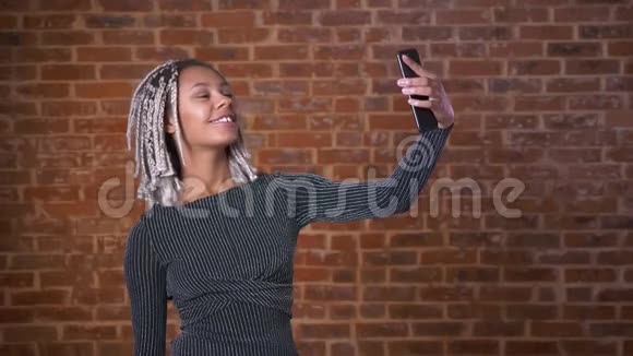 年轻的非洲女孩与可怕的使用智能手机自拍微笑砖墙的背景视频的预览图