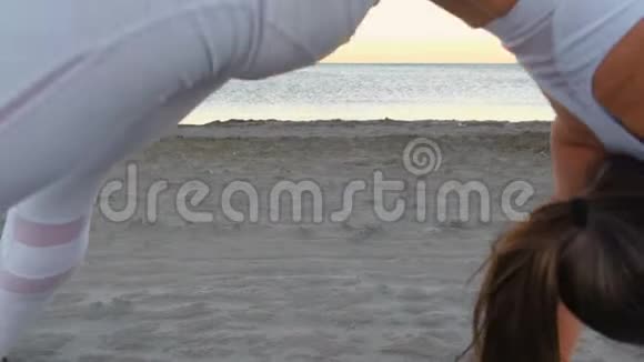 年轻女子在日出时在沙滩上做瑜伽伸展Chakrasana轮式软管视频的预览图