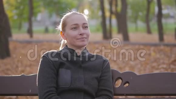 一个女人坐在城市秋天花园的长凳上视频的预览图