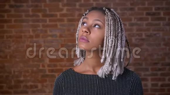 年轻的非洲女孩带着可怕的目光思考和微笑背景中的砖墙视频的预览图