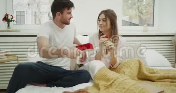 一对夫妇庆祝某件事早上男人给他的女人留下了深刻的印象把礼物放在床上视频的预览图