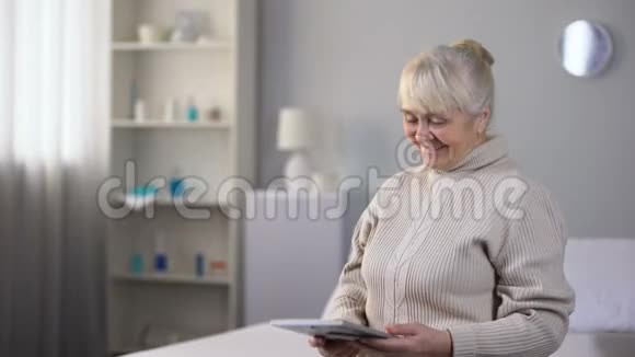 快乐的老太太独自坐着看着照片愉快的家庭回忆视频的预览图