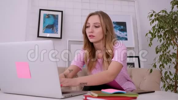 一个漂亮迷人的女孩穿着一件粉红色的t恤金发碧眼穿着一件明亮的笔记本电脑视频的预览图