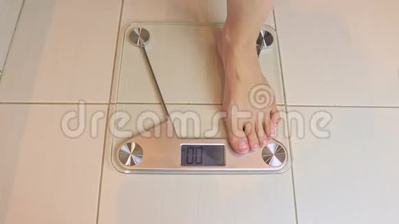 女人光着脚站在秤上在浴室里称重秤显示674公斤饮食和减肥视频的预览图