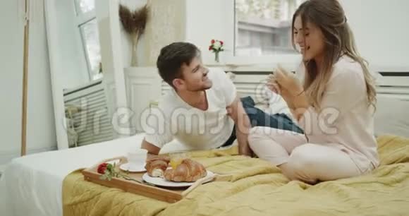 夫妻在床上吃早餐吃有趣的法国羊角面包并在他们舒适的卧室里度过美好的时光视频的预览图