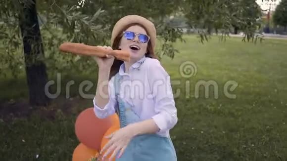 在夏天的公园里嬉皮士女孩用法国面包当麦克风唱歌野餐视频的预览图