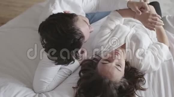 头顶射中幸福的年轻夫妇躺在床上谈特写俯视令人放松的男人和女人慢动作视频的预览图