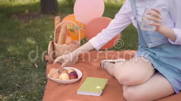 年轻的姜姑娘在夏天的公园里吃牛角面包喝果汁野餐视频的预览图