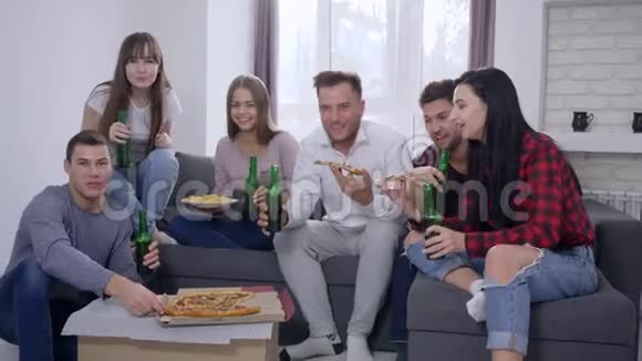 家庭聚会公司青年朋友在房间里坐在沙发上看电视时吃披萨喝啤酒视频的预览图