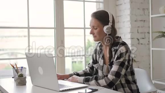 年轻的女企业主设计师一边在笔记本电脑上工作一边在耳机里听音乐售货员视频的预览图