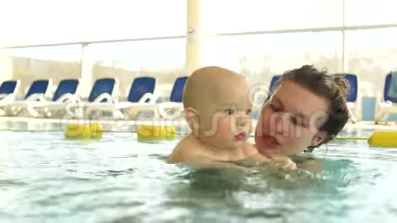 妈妈教她的孩子在一个封闭的公共游泳池里游泳孩子犹豫地摆手孩子的发展母亲视频的预览图