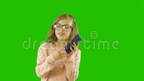 一个六岁十岁的小女孩长着卷曲的长锁在她的手中唤醒了电话并开始清晰地表达她和视频的预览图