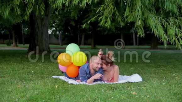 一对漂亮的夫妇躺在铺在绿草上的白色毯子上在茂密的树叶下闲聊着视频的预览图