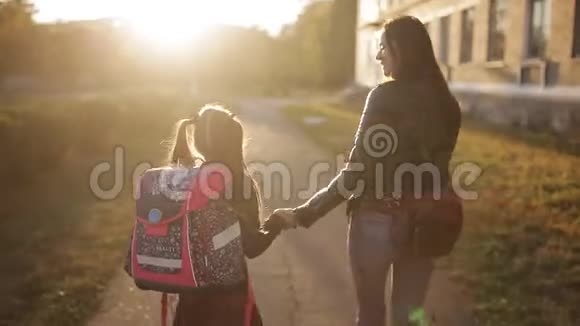 母亲和女儿在日落时从学校回来妈妈和女儿背着一个公文包回家视频的预览图