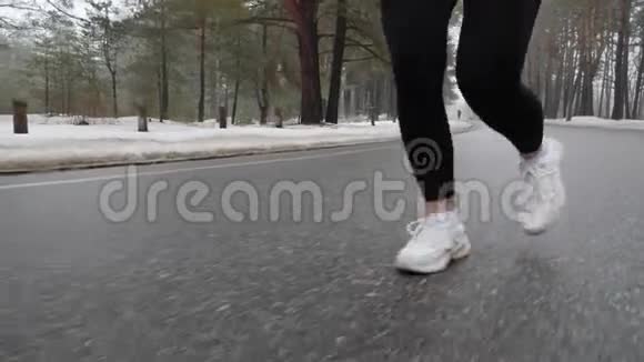 年轻迷人的白种人女孩在冬天带着耳机在雪地公园跑步特写双腿前跟射击慢动作视频的预览图