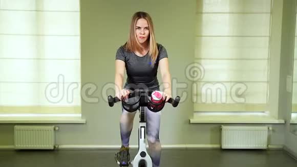 在健身房骑自行车来适应年轻女人强壮的女运动员在健康俱乐部做循环有氧运动视频的预览图