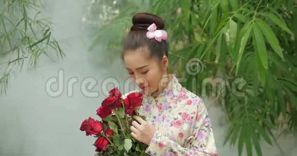 迷人的亚洲女人穿着传统服装带着一束红色玫瑰花望着镜头微笑着视频的预览图