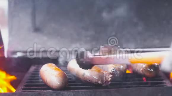 四个猪肉多汁的猪肉香肠是在热烤架上炸的他们用钳子翻过来很多烟和火特写镜头慢一点视频的预览图