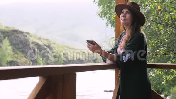 戴着帽子穿着白衬衫戴着豌豆的漂亮黑发女人在手机上聊天在手机上自拍享受着视频的预览图