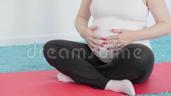 一个怀孕的女孩正在做瑜伽冥想肚子里的婴儿推着一个女人抚摸她的腹部视频的预览图