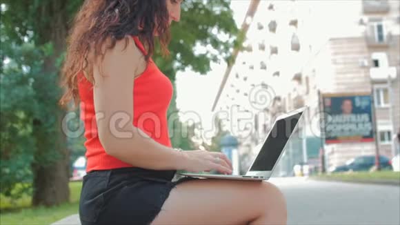 在笔记本电脑上工作的女人穿着黑色短裤和笔记本电脑在公园里工作的漂亮黑发女人女孩在她的身上打印视频的预览图