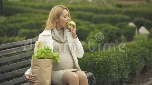 微笑着期待着女士在长凳上吃新鲜苹果和购物袋医疗保健视频的预览图