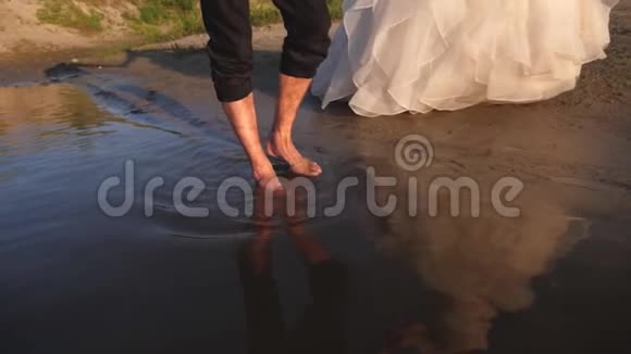 新郎是赤脚的新娘穿着一件白色的衣服沿着河边走恋爱中的一对情侣走在视频的预览图