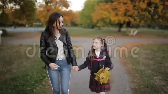 妈妈和一个小女孩肩上背着背包手里拿着一束黄色的秋叶从家里回来视频的预览图