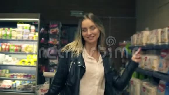 在超市里快乐的年轻女人在货架上通过化妆品和奶制品跳舞近景视频的预览图