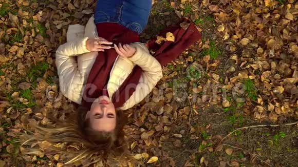 年轻迷人的女孩躺在秋天公园的叶子上手里拿着树上的树枝视频的预览图