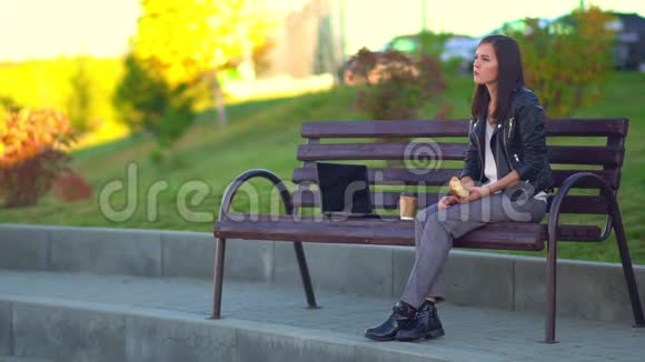 公园里的女孩坐在长凳上下班休息做零食吃烤饼视频的预览图