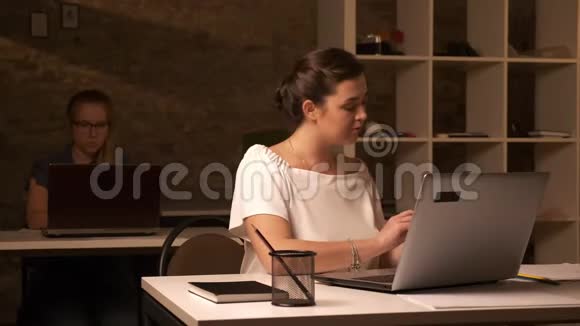一位严肃的白种人女商人正在看着她的电脑和工作场所的人进行电话交谈视频的预览图