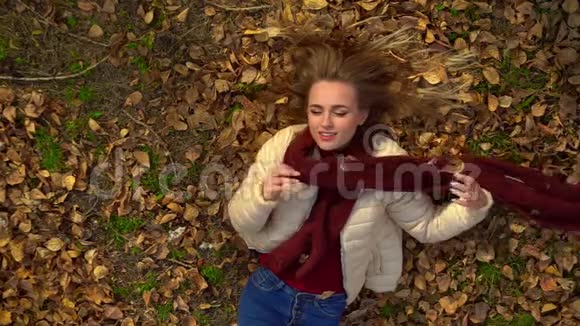 美丽的女孩模特躺在秋叶上微笑调情看着镜头视频的预览图