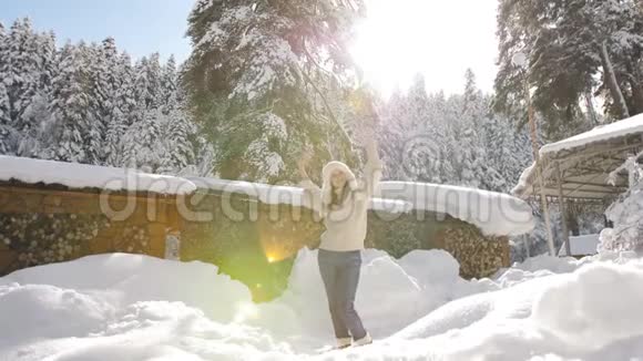 穿着针织毛衣和毛皮帽的漂亮女孩在小屋附近享受阳光明媚的冬日视频的预览图