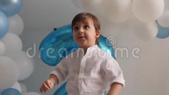 两岁的男孩穿着白色衬衫穿着蓝色气球坐在家里视频的预览图