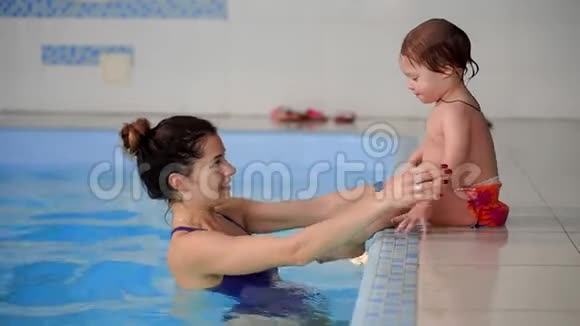 在游泳池里婴儿从旁边跳到水里慢慢地游向母亲视频的预览图