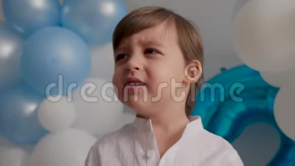 两岁的男孩穿着白色衬衫穿着蓝色气球坐在家里视频的预览图